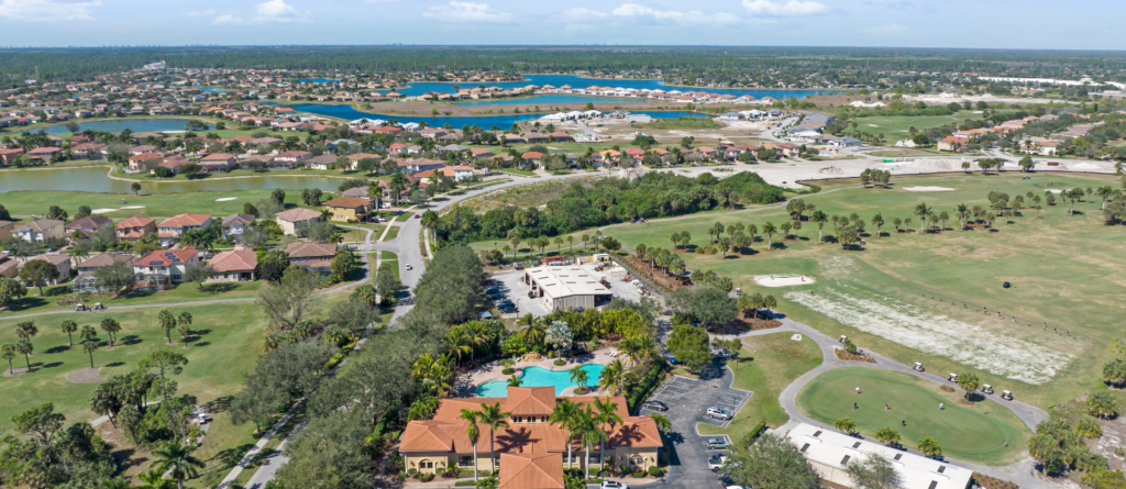 Aerial view over Valencia Golf & Country Club in Naples, Florida, with the clubhouse and pool in the foreground and golf fairways, homes and lakes beyond